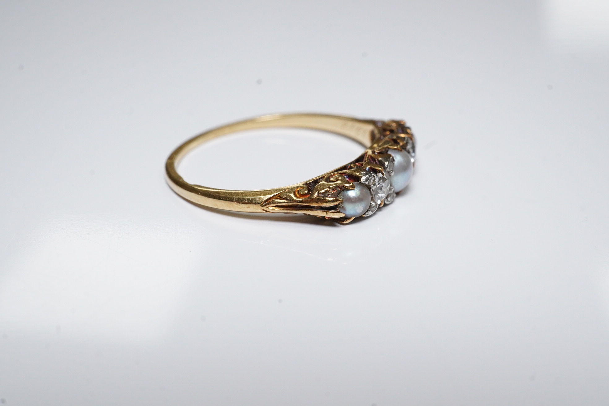 An early 20th century yellow metal (stamped 18), two stone diamond and three stone split pearl set half hoop ring, size O, gross weight 2.2 grams. Condition - fair